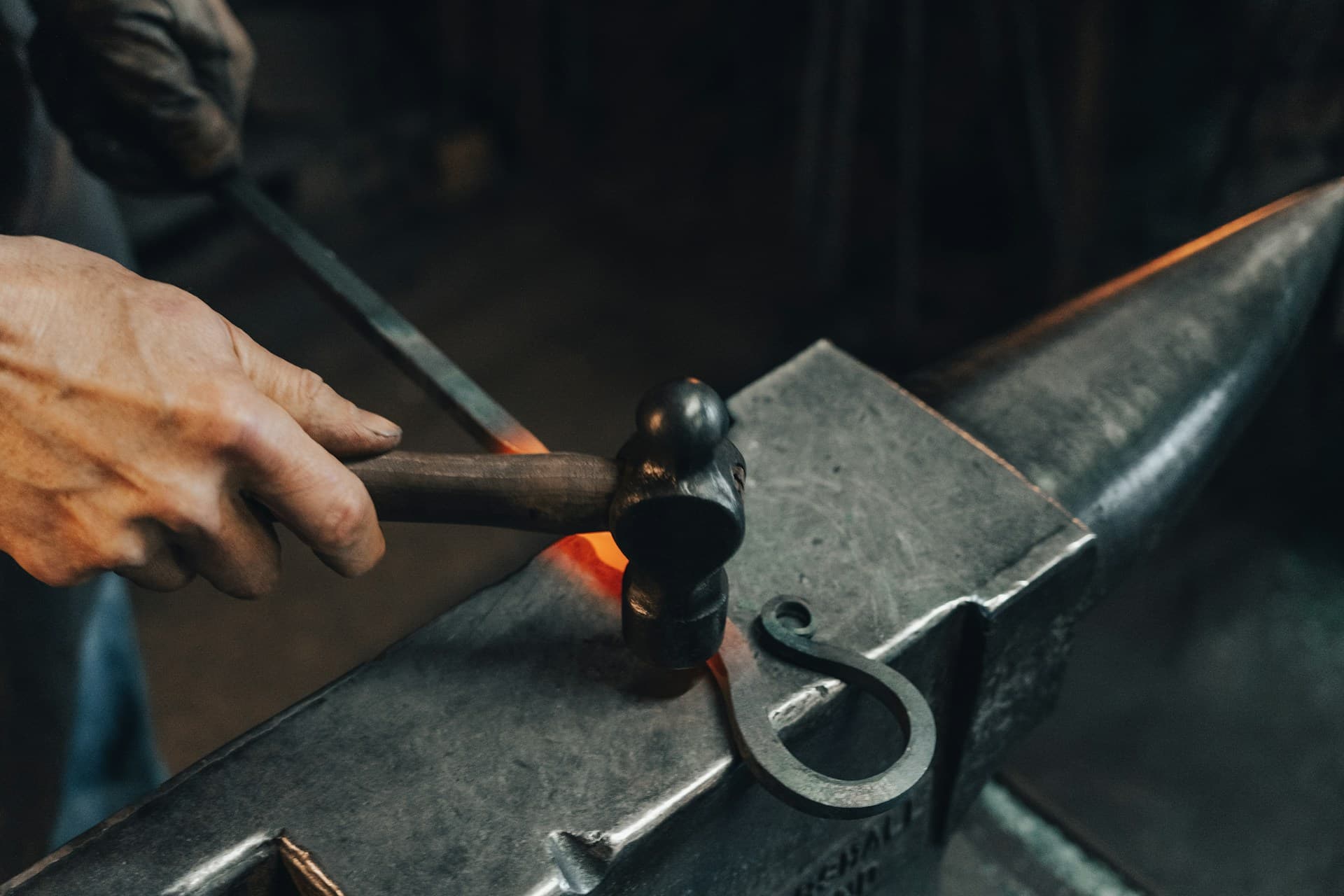 Photo of a person hammering a red hot metal piece on an anvil.