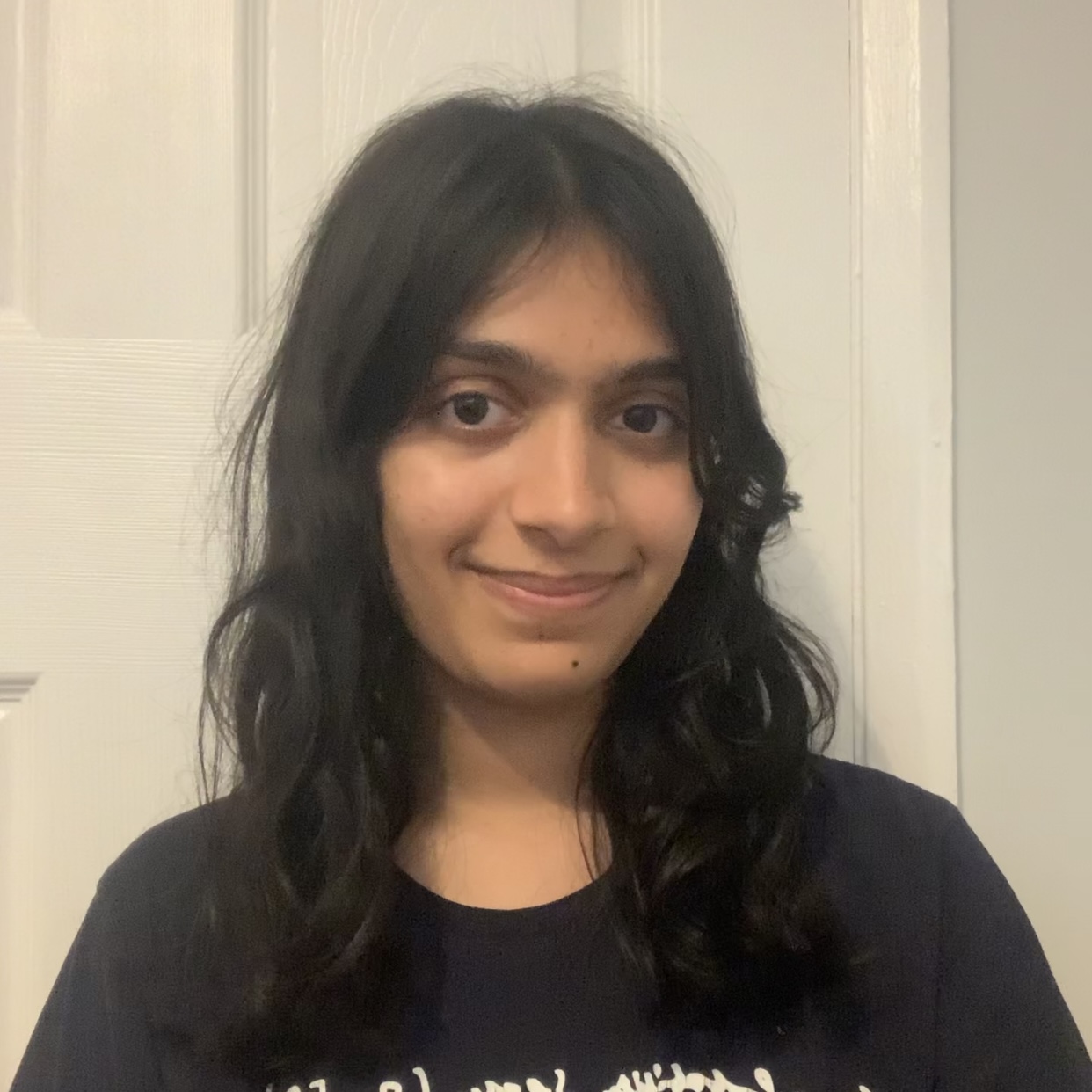 Anushka, wearing a black t-shirt, smiling at the camera, over a white background.