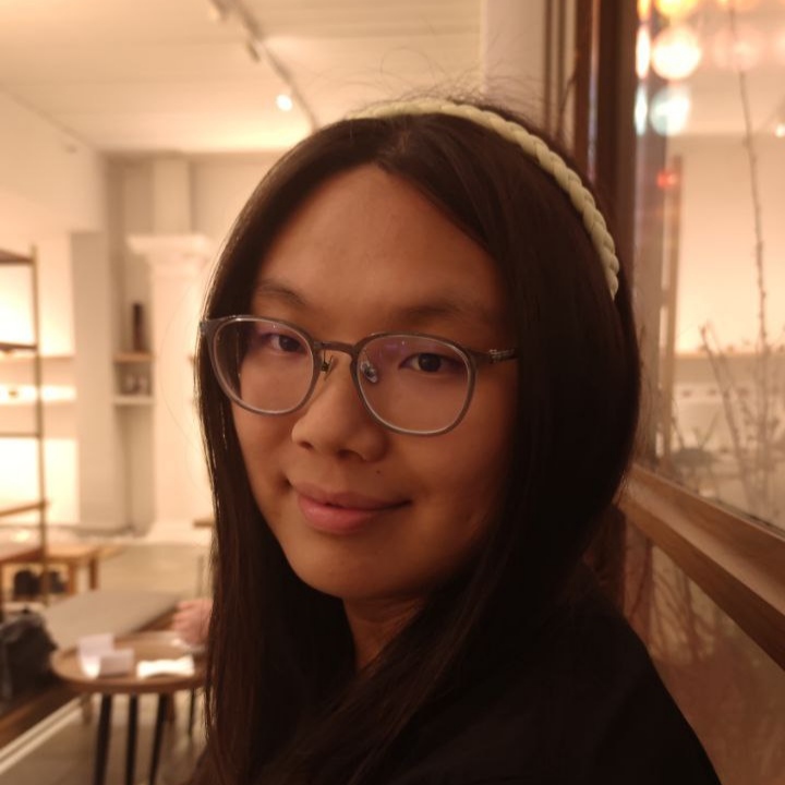 Jules looking at the camera, with soft indoor lighting behind her. She is wearing glasses and a white tiara over her dark long hair.